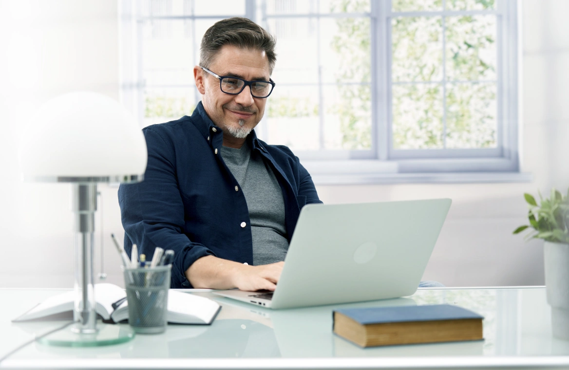 A man with glasses using a laptop in his home office to create a Frontier account online