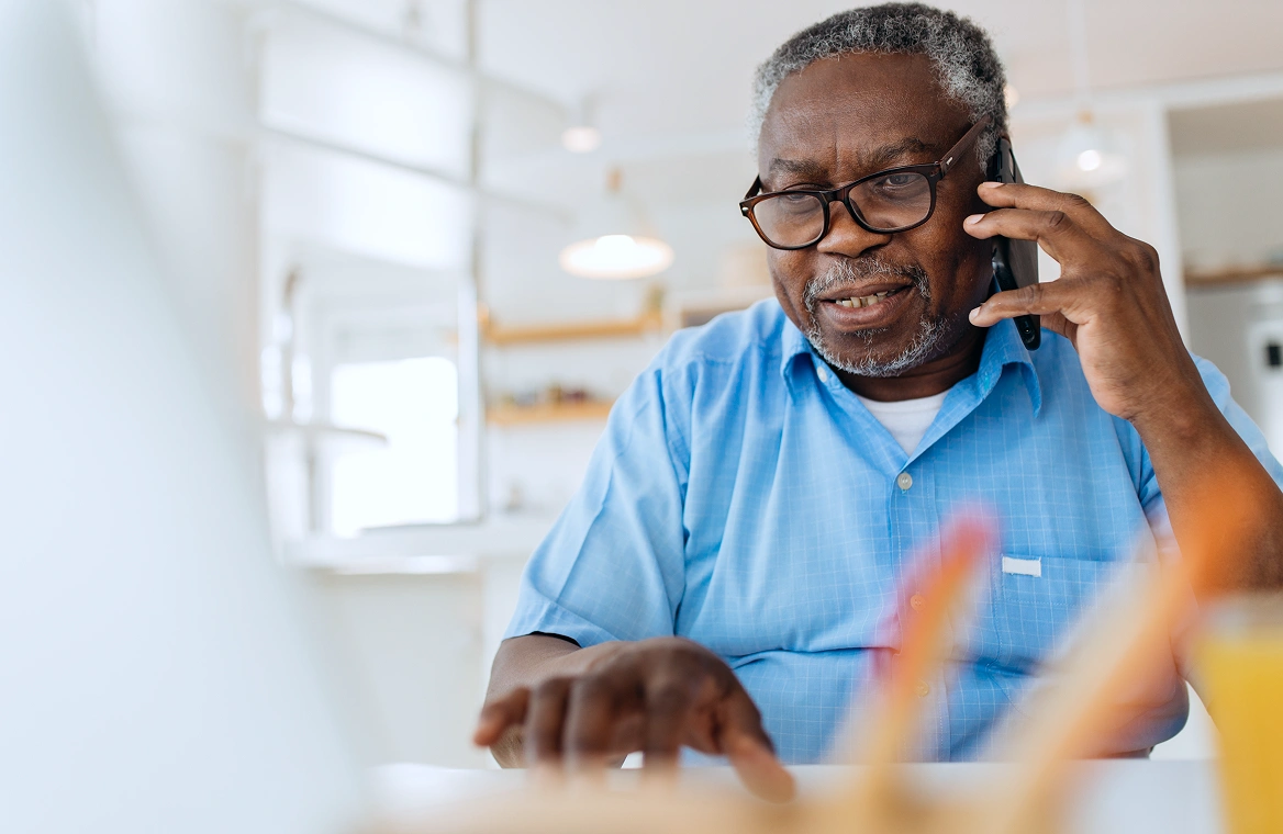 An older gentleman using a computer and on the phone with customer service